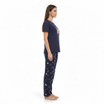 A woman stands in profile wearing a navy blue pajama set with a butterfly graphic on the top and a navy blue pajama pant with a light pink butterfly pattern, against a plain white background.