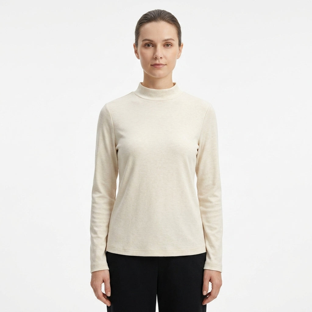 A woman modeling a long-sleeve mock neck knit top in a light cream color, paired with black pants, against a plain white studio background.