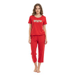 A woman modeling a red two-piece pajama set consisting of a short-sleeve t-shirt with a heart pattern on the chest and matching red cropped pants, shot against a plain white background.