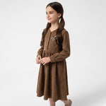 A young girl wearing a JOANNA FASHION brown corduroy long sleeve dress with a rose floral appliqué on the chest.