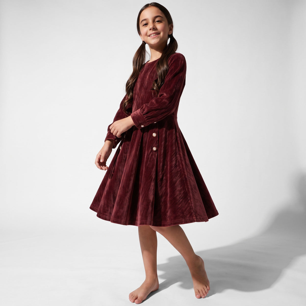 JOANNA FASHION girls long sleeve burgundy corduroy dress with button detail on a smiling girl