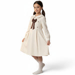 JOANNA FASHION girl wearing a cream textured long-sleeve dress with a Peter Pan collar and brown bow detail.