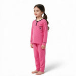A young girl wearing a JOANNA FASHION pink long-sleeve pajama set with black polka dots and heart pocket detail.