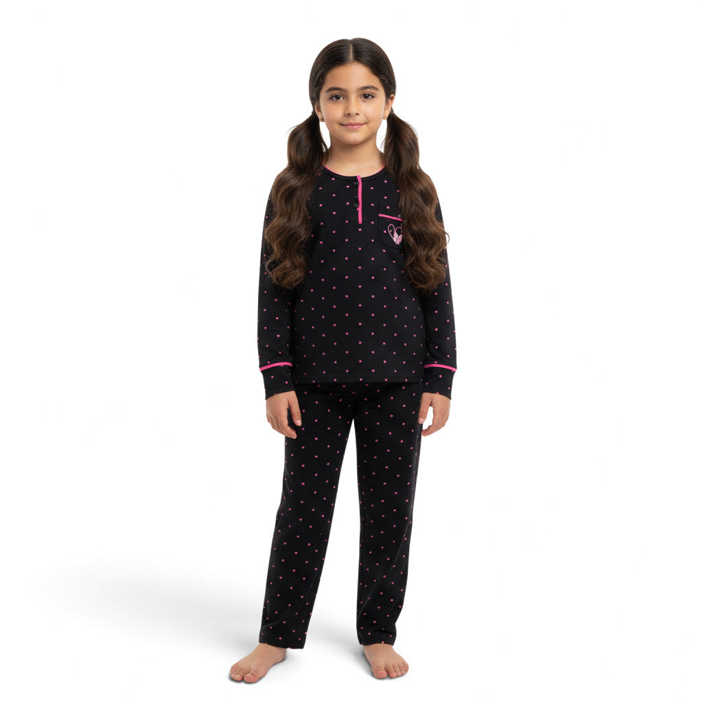 A young girl wearing a JOANNA FASHION black long-sleeve pajama set with pink polka dots and heart pocket detail.