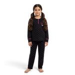 A young girl wearing a JOANNA FASHION black long-sleeve pajama set with pink polka dots and heart pocket detail.