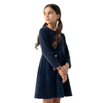 A young girl wearing a JOANNA FASHION navy blue long-sleeve corduroy dress with white button details at the waist.