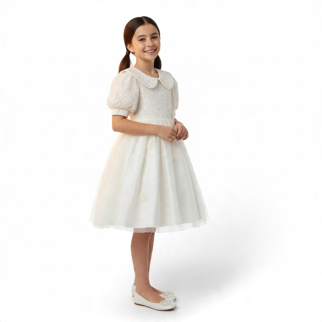 A young girl smiling in a white JOANNA FASHION formal dress with a lace bodice, puff sleeves, and a tulle skirt.