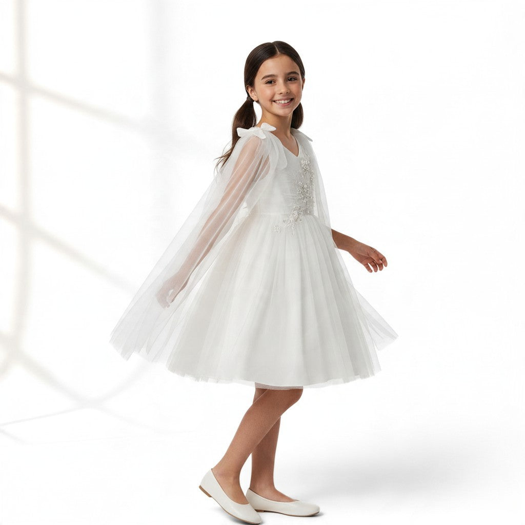 JOANNA FASHION white tulle flower girl dress with floral embroidery, beadwork, and an attached sheer cape with bows.