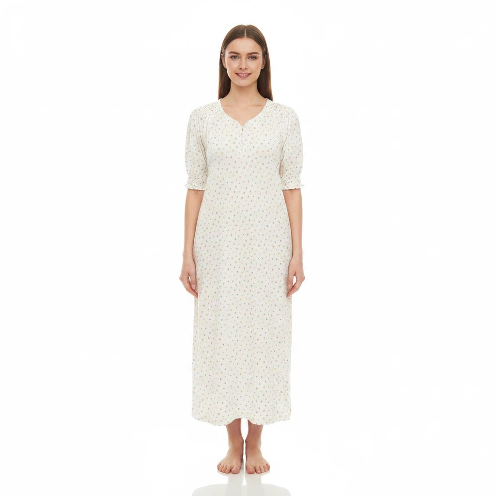 A woman modeling a long-sleeved, knee-length nightgown with a small floral print on a cream background, standing against a plain white studio background.