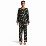 A woman stands barefoot against a plain white studio background wearing a long-sleeve pajama set with a black base and an allover beige floral print.