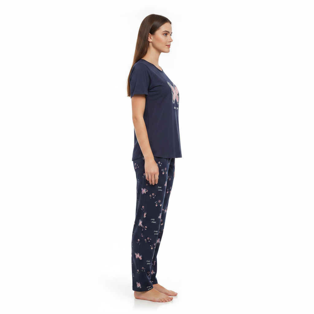 A woman stands in profile wearing a navy blue pajama set with a butterfly graphic on the top and a navy blue pajama pant with a light pink butterfly pattern, against a plain white background.