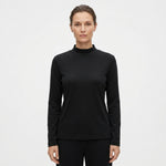 A woman modeling a black long-sleeve mock neck top against a plain white studio background.