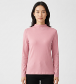 A woman modeling a light pink long-sleeve mock neck top against a plain white studio background.