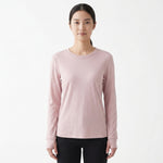 A woman modeling a light pink long-sleeve crewneck shirt against a plain white studio background.