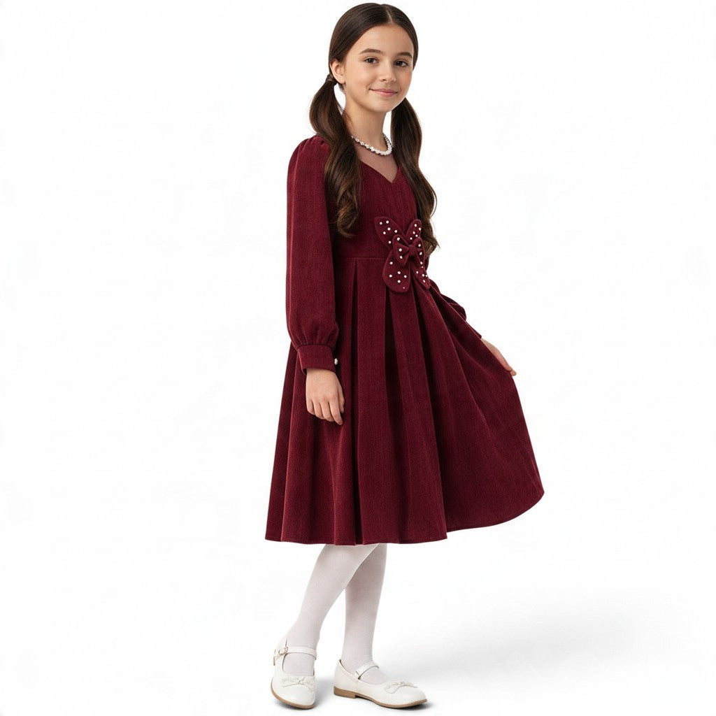 JOANNA FASHION girl in a burgundy corduroy long-sleeve pleated dress with a pearl-embellished butterfly waist detail.