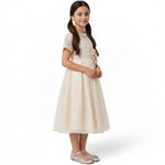 JOANNA FASHION girl wearing a champagne formal dress with a lace bodice, tulle skirt, and a large waist flower.