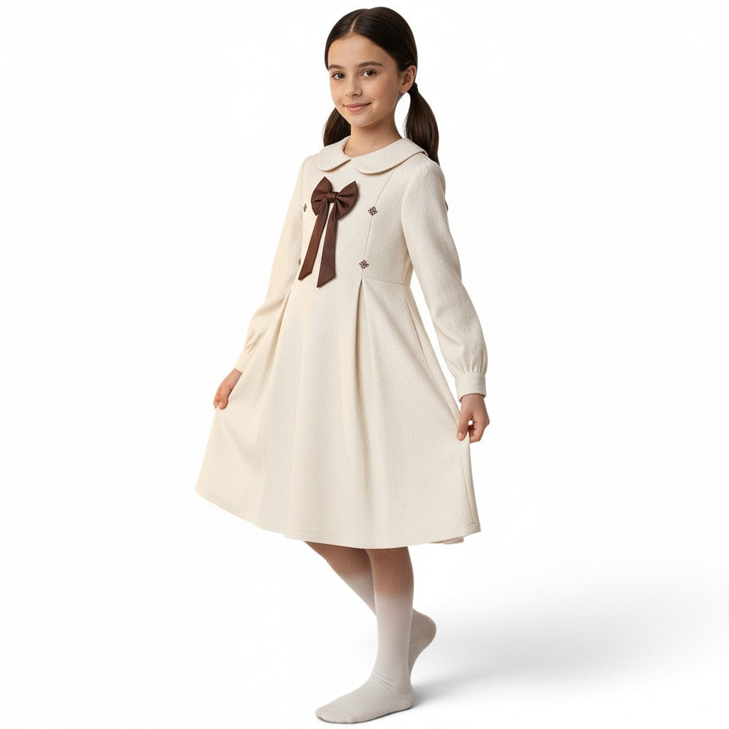 JOANNA FASHION girl wearing a cream textured long-sleeve dress with a Peter Pan collar and brown bow detail.