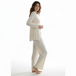 A woman wearing a JOANNA FASHION three-piece cream ribbed loungewear set with a cardigan, camisole, and wide-leg pants.