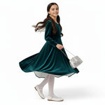 JOANNA FASHION girl in a deep emerald green velvet high-low dress with sparkling bodice and pearl trim, twirling.