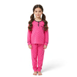 A young girl wearing a JOANNA FASHION pink long-sleeve pajama set with black polka dots and heart pocket detail.