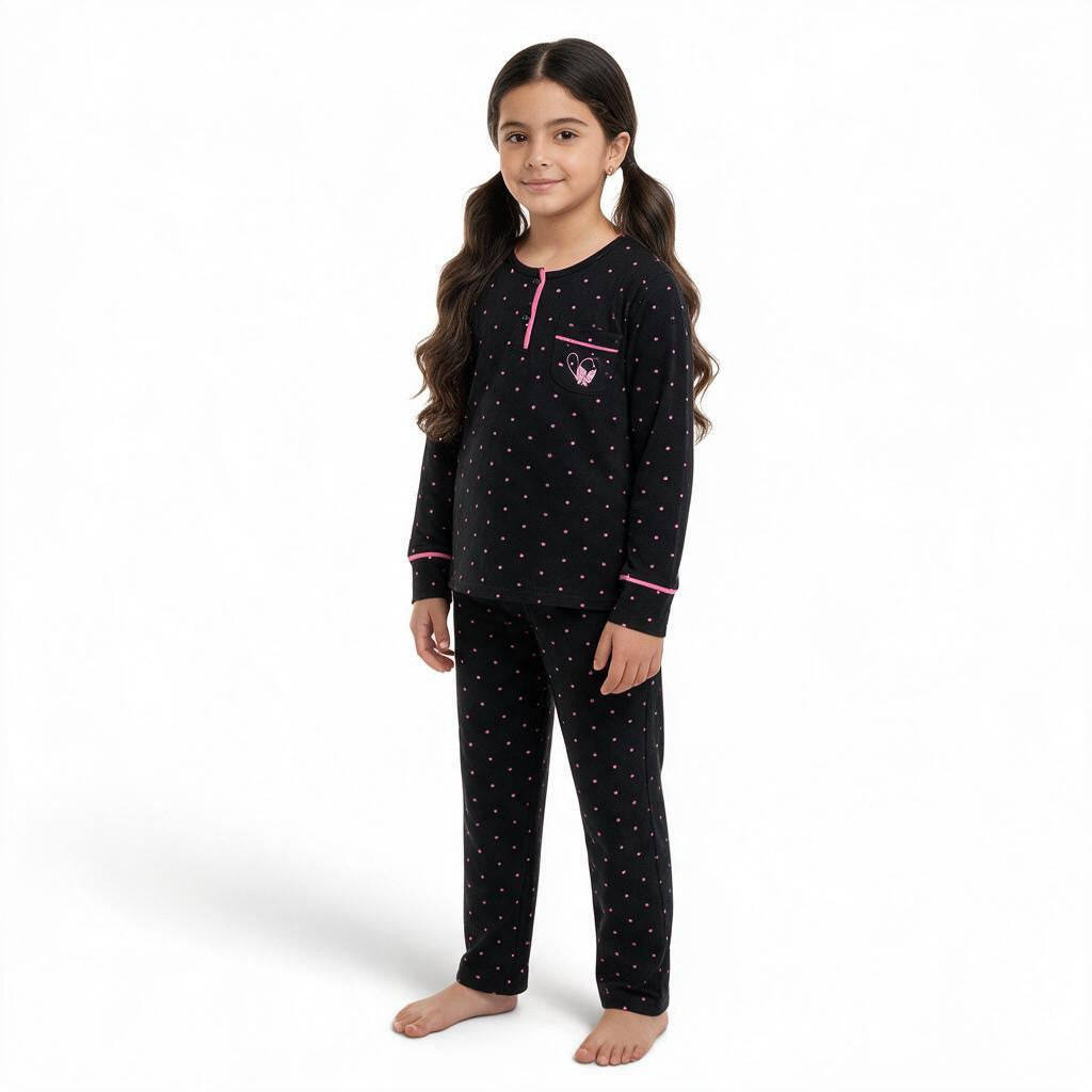A young girl wearing a JOANNA FASHION black long-sleeve pajama set with pink polka dots and heart pocket detail.