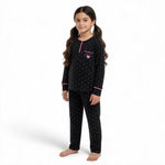 A young girl wearing a JOANNA FASHION black long-sleeve pajama set with pink polka dots and heart pocket detail.