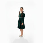 JOANNA FASHION girl wearing a dark green velvet dress with puff sleeves and pearl trim, standing against white background