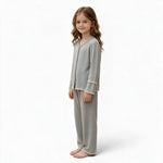 A young girl wearing a JOANNA FASHION grey long-sleeve button-down pajama set with delicate scalloped lace trim.