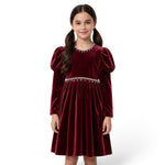 JOANNA FASHION girl wearing a deep red velvet dress with puff sleeves and pearl-style trim at the neckline and waist.