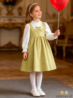JOANNA FASHION sage green quilted pinafore dress with bow detail worn by a girl holding a red balloon
