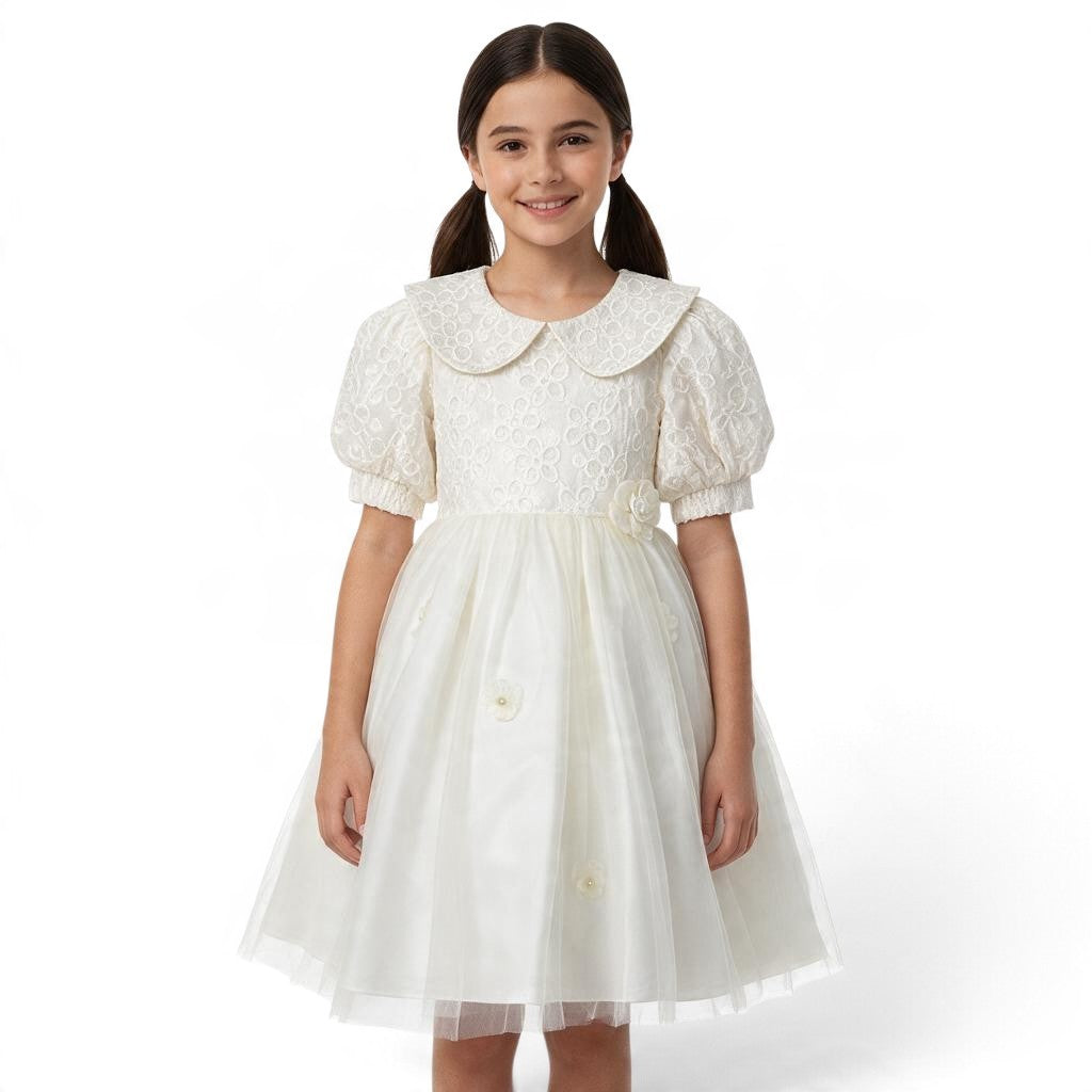 A young girl wearing a white JOANNA FASHION formal dress with a lace bodice, peter pan collar, and tulle skirt.